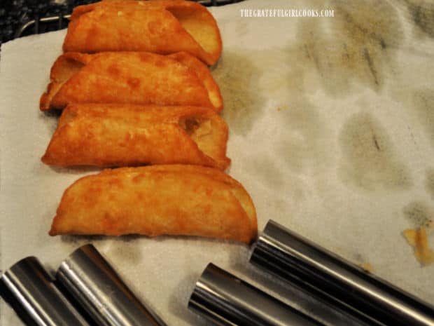 Metal cannoli tubes are removed from fried shells, cooling and draining on paper towels.