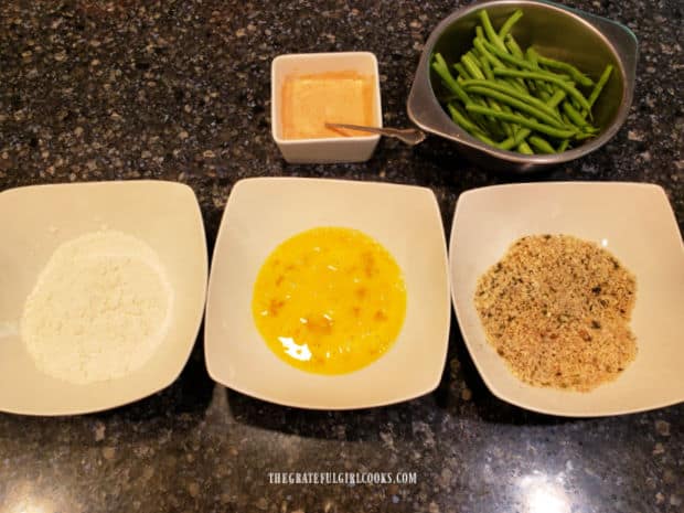 Dipping station with bowls of flour, egg, and panko mixture for dredging fresh green beans.