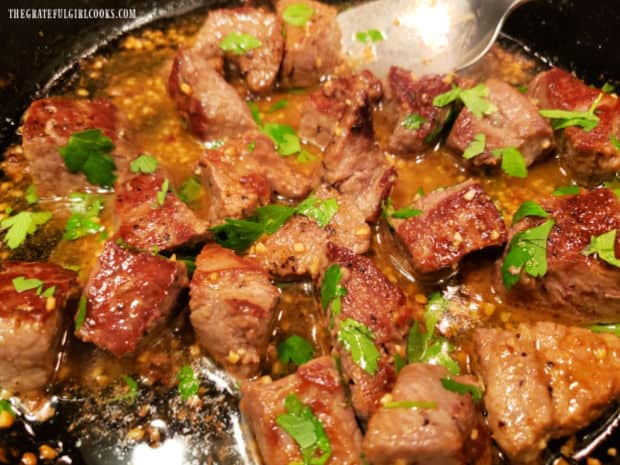 Easy garlic butter steak bites are topped with chopped parsley before serving hot.