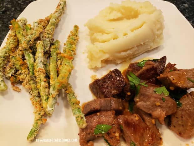 A white plate with easy garlic butter steak bites, mashed potatoes and crispy green bean fries.