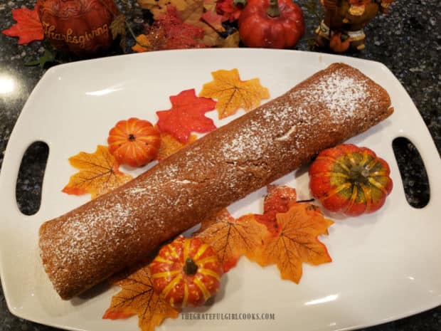 The pumpkin cream cheese roll is sprinkled with powdered sugar before slicing to serve.