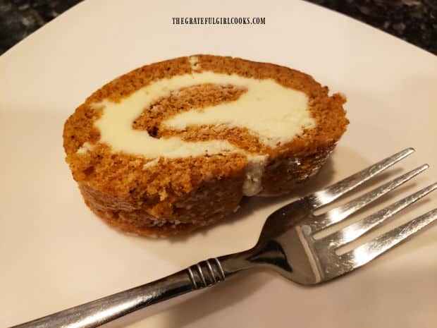 A slice of the pumpkin cream cheese roll reveals the spiraled cream cheese filling inside.