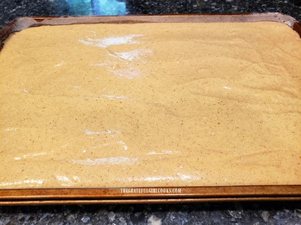 Pumpkin roll batter is spread in a large greased/floured cookie sheet.