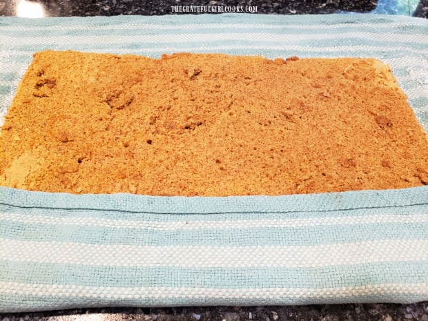 The damp dish towel is rolled up into the pumpkin cake to form a long roll.