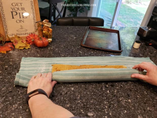 Finishing rolling up the damp dish towel and pumpkin cake into a log shape, before it rests.