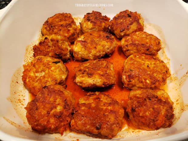 Browned meatballs are place in single layer in a baking dish with enchilada sauce on the bottom.