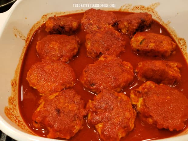 Red enchilada sauce is poured on top of the chicken enchilada meatballs in dish.