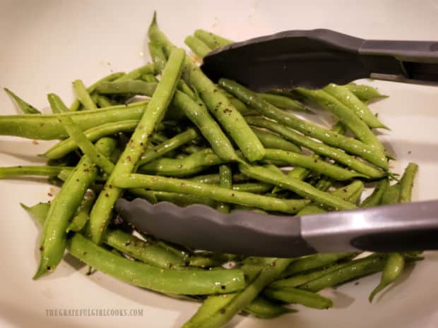 Fresh green beans are tossed with olive oil, seasoning salt and pepper until coated.