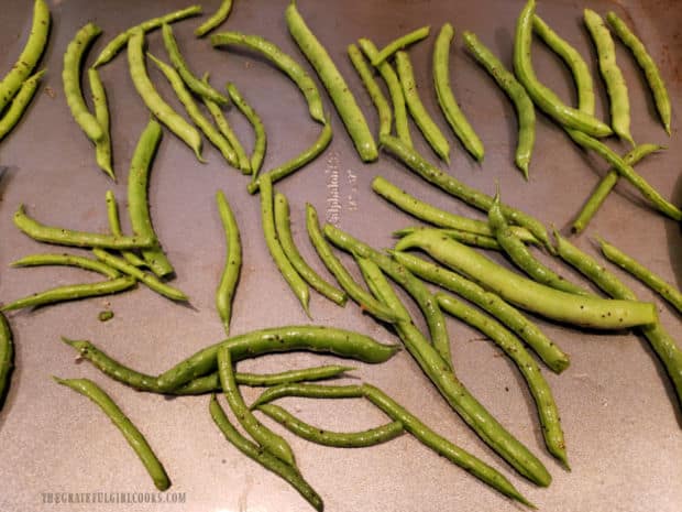 Oven roasted green beans are placed on baking sheet in a single layer for baking.