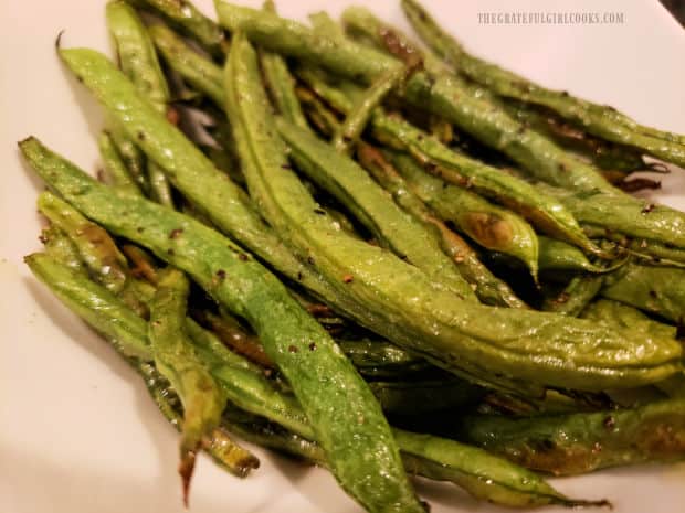 Oven roasted green beans, are served hot in a white bowl, after baking is done.