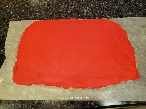 Red dough for the peppermint pinwheel cookies is fitted on top of the plain dough layer.