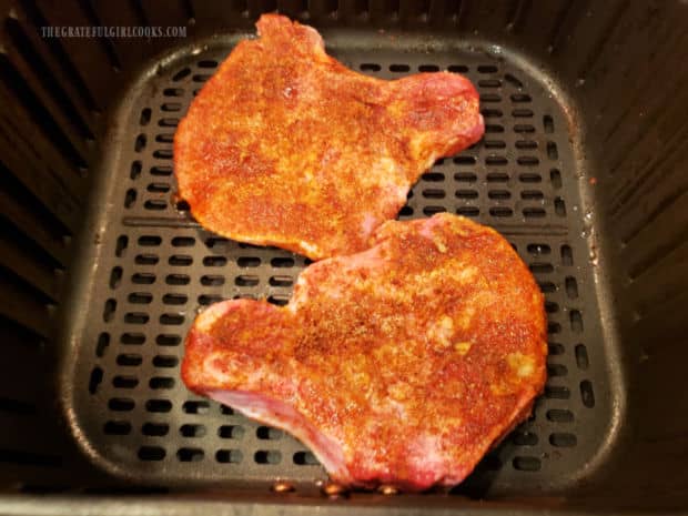 Well seasoned pork chops are placed in basket of air fryer in one layer.
