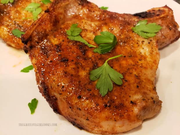 A close up of one of the air fryer pork chops, with parsley garnish, on a white plate.