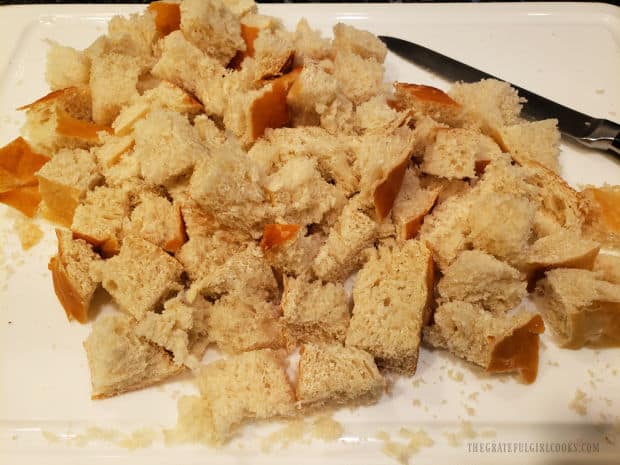 A half loaf of French bread is cut into small cubes.