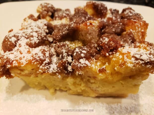 After cooling slightly, baked eggnog French toast is sprinkled with powdered sugar and sliced.