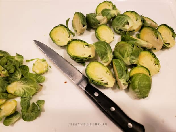 Brussels sprout ends are trimmed, then the sprouts are sliced in half.