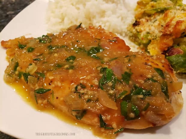 A plate with one of the chicken cutlets in pan sauce, served with rice and a veggie.