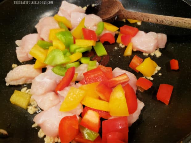 Chunks of chicken breast and green, yellow and red bell peppers are added to the skillet.