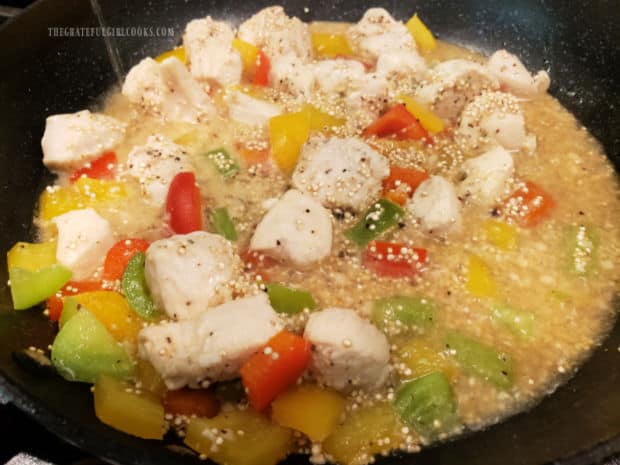 Quinoa and water are added to the chicken and veggies in the skillet.