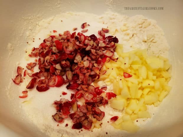 Chopped cranberries and peeled apples are added to the flour and butter mixture in bowl.