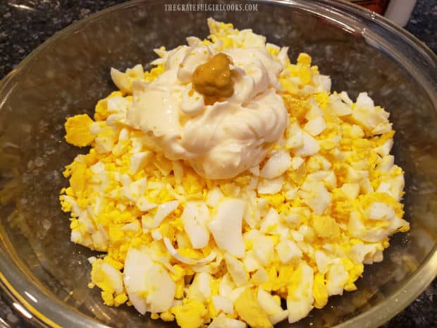 Mayonnaise and a small amount of yellow mustard are added to the eggs in bowl.