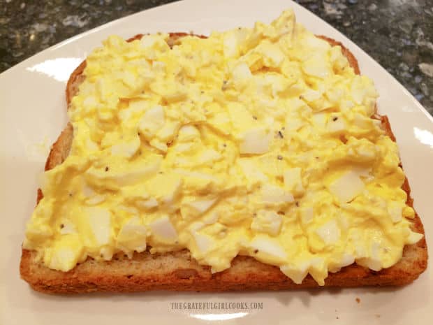 A slice of bread is covered with a layer of cold egg salad.