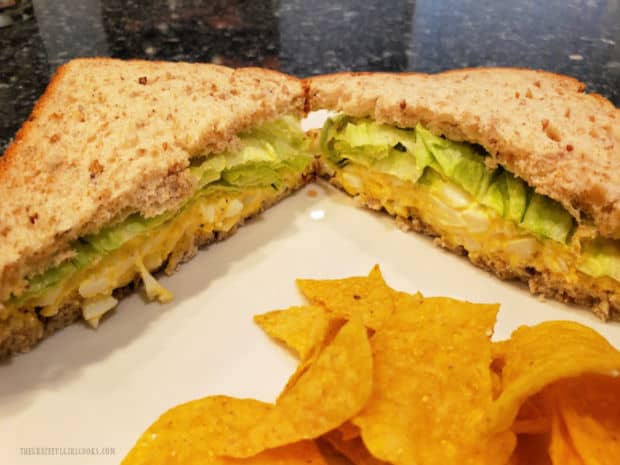Egg salad sandwich is served, cut in half on a white plate, with tortilla chips on the side.