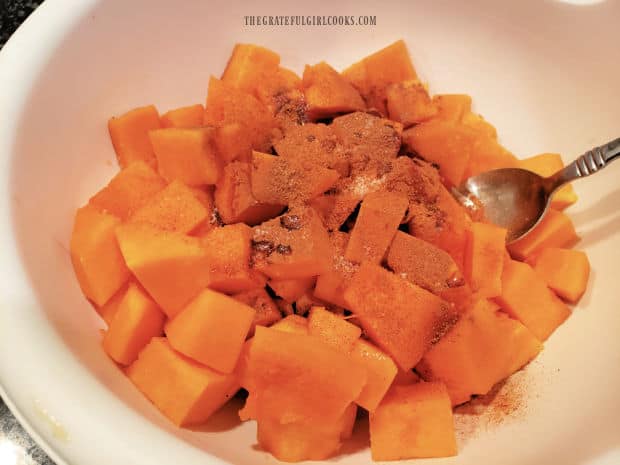 Spices, maple syrup and oil are added to the cubed butternut squash in a large bowl.