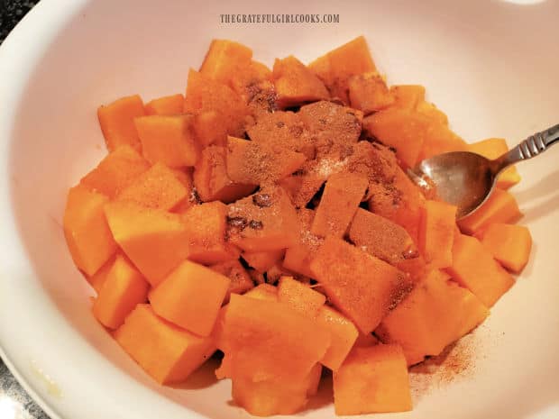 Spices, maple syrup and oil are added to the cubed butternut squash in a large bowl.