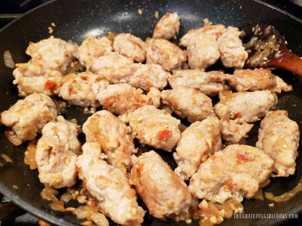 A skillet of fully cooked chicken Italian sausage chunks, with onions and minced garlic.