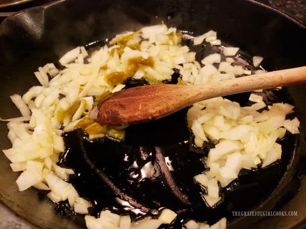Chopped onion and jalapeño pepper are cooked in hot oil in a cast iron skillet.