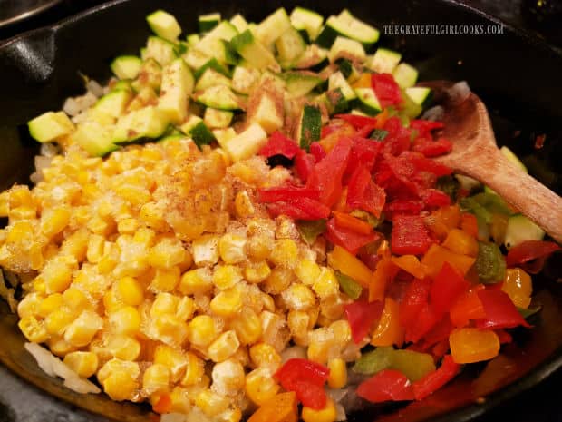 Frozen corn, bell peppers, zucchini and spices are added to the hot skillet.