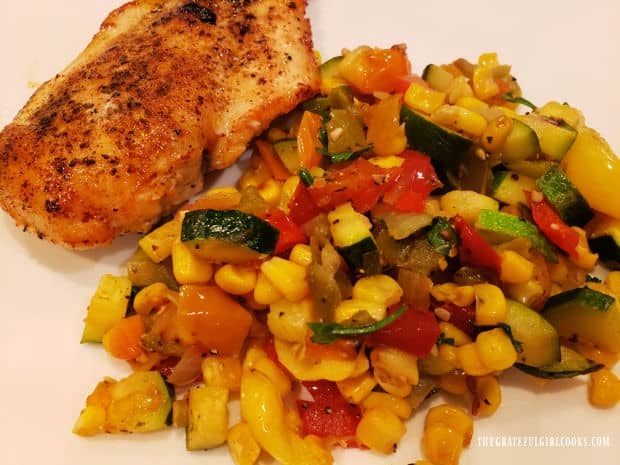 Southwest Veggie Skillet side dish is served with a cooked chicken breast, on a white plate.