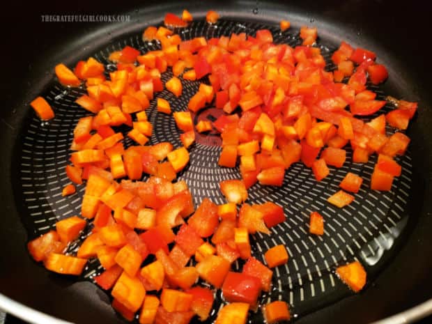 Red bell peppers and carrots are cooked in oil until softened, in a large skillet.