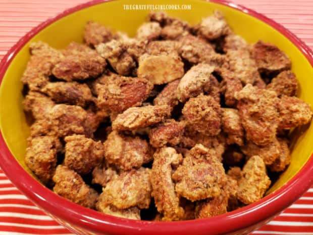 A yellow bowl with red trim, full of cinnamon glazed almonds, ready to be eaten.