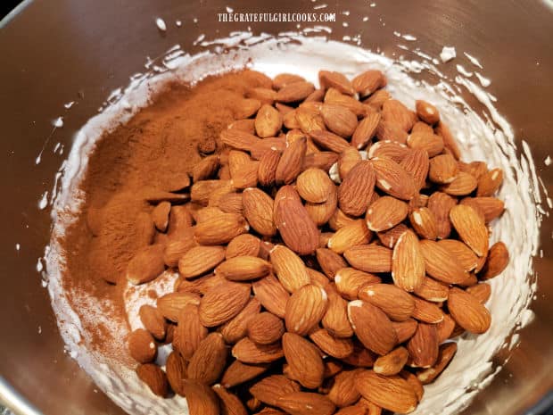 Almonds and ground cinnamon are added to the stiff egg white mixture in the bowl.