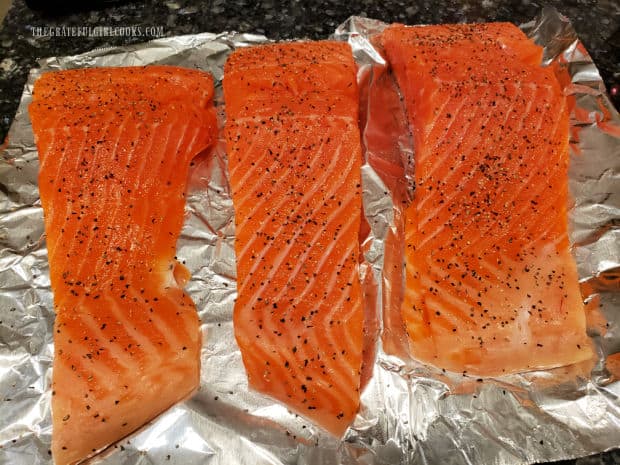 Three steelhead trout fillets are seasoned with salt and pepper before cooking.