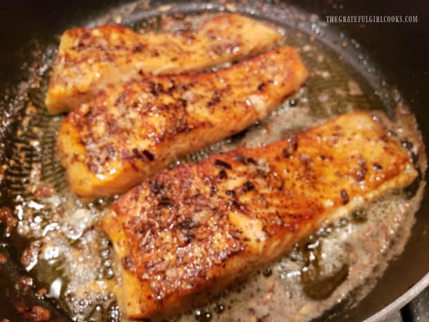 Pan-seared steelhead trout fillets are browned and drizzled with brown butter sauce in skillet.