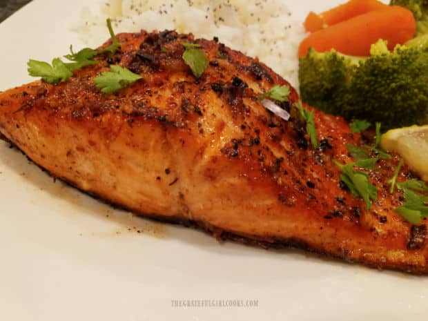 A piece of steelhead trout, garnished with lemon slice and chopped fresh parsley to serve.