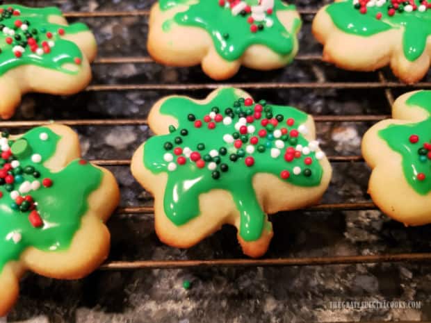 Shamrock cookies, with green icing and colored sprinkles, resting on a wire rack.