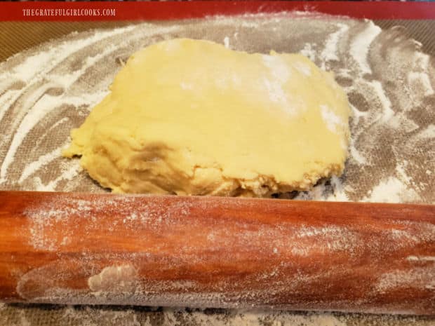 Cookie dough is halved, then each piece is rolled out on a floured surface until 1/4" thick.