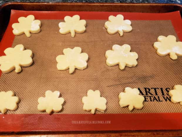 Cut out shamrock cookies on a silicone mat (on baking sheet) ready to be baked.