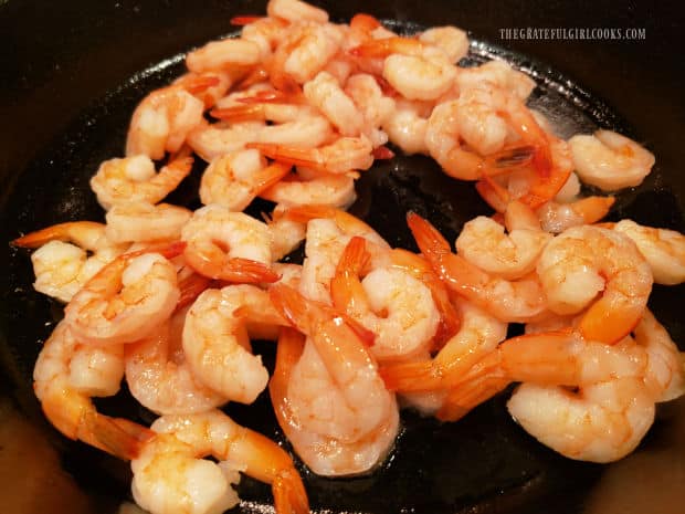 Large shrimp are stir-fried in hot oil in a black skillet.