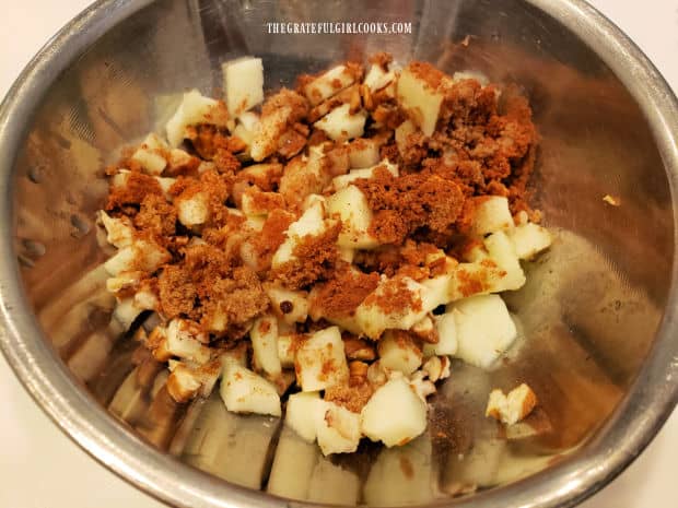 Peeled, diced apples are mixed with lemon juice, brown sugar, cinnamon and pecans in a bowl.