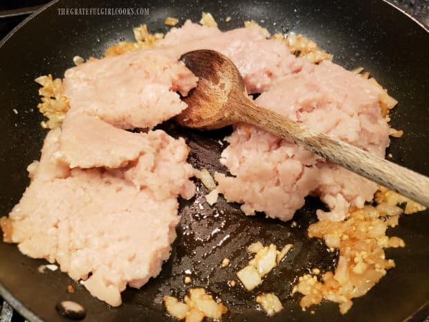 Ground chicken is added to the skillet and broken up with a wooden spoon into small pieces.