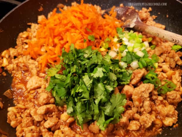 Grated carrots, chopped cilantro and green onions are added to the skillet.