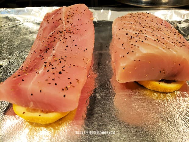 Seasoned mahi mahi fillets placed on top of lemon slices on a foil-covered baking sheet.