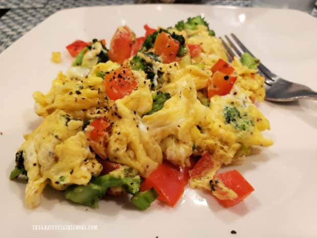 A white plate with one serving of egg, bacon and veggie scramble.