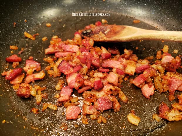 Spices and minced garlic are combined with cooked bacon and onions in skillet.