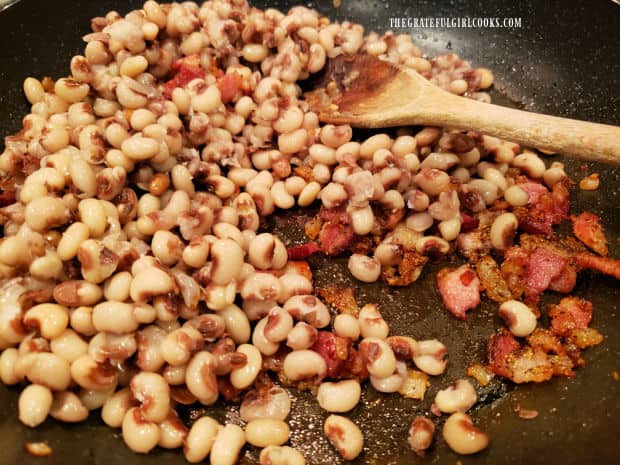 Cooked blackeyed peas are stirred into bacon and onion mixture in the skillet.